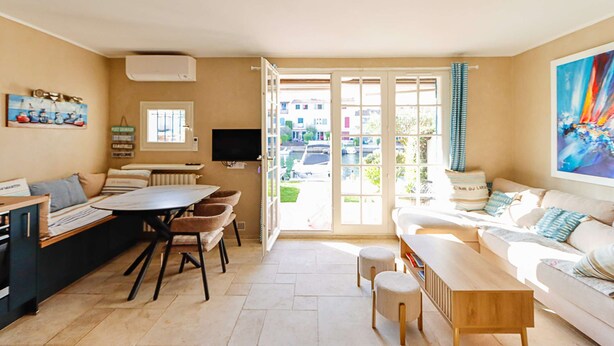 A living room with a sofa, a coffee table, a TV, and a dining area with chairs and a table. - PORT GRIMAUD: Superb 3-room apartment - A/C, terrace and garden (PORT GRIMAUD)
