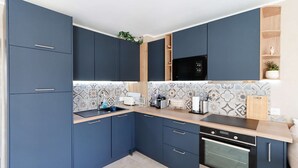 A modern kitchen with dark blue cabinets, a microwave, a stove, and a tiled backsplash. - PORT GRIMAUD: Superb 3-room apartment - A/C, terrace and garden (PORT GRIMAUD)