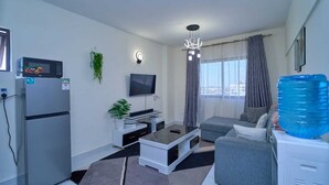 A modern living room with a flat-screen TV, a refrigerator, a coffee table, a sofa, and a water dispenser. - Adorable 1-bedroom bed & breakfast in lively Nairobi (Nairobi)