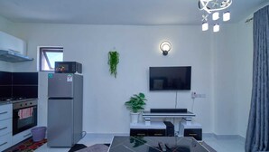 A modern kitchen with a refrigerator, stove, and microwave. There is a dining area with a table and chairs, a flat-screen TV mounted on the wall, and a ceiling light fixture. - Adorable 1-bedroom bed & breakfast in lively Nairobi (Nairobi)