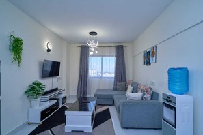 A modern living room with a flat-screen TV, a sofa, a coffee table, a water dispenser, and a ceiling light fixture. - Adorable 1-bedroom bed & breakfast in lively Nairobi (Nairobi)