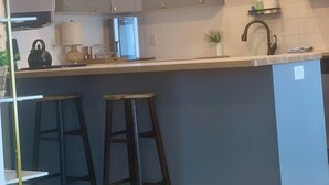 A kitchen with a central island, bar stools, a refrigerator, and a pendant light fixture.