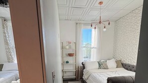 Un dormitorio con cama, mesita de noche, cómoda y ventana con cortinas.