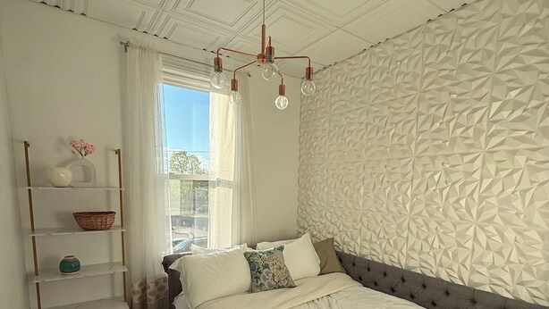 A bedroom with a bed, a shelf with decorative items, a patterned rug, and a textured wall.