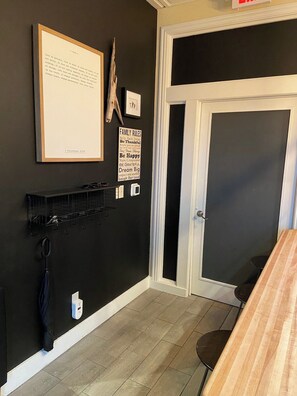 A room with a black wall, a framed text on the left, a door with a white frame, and a small shelf with items.