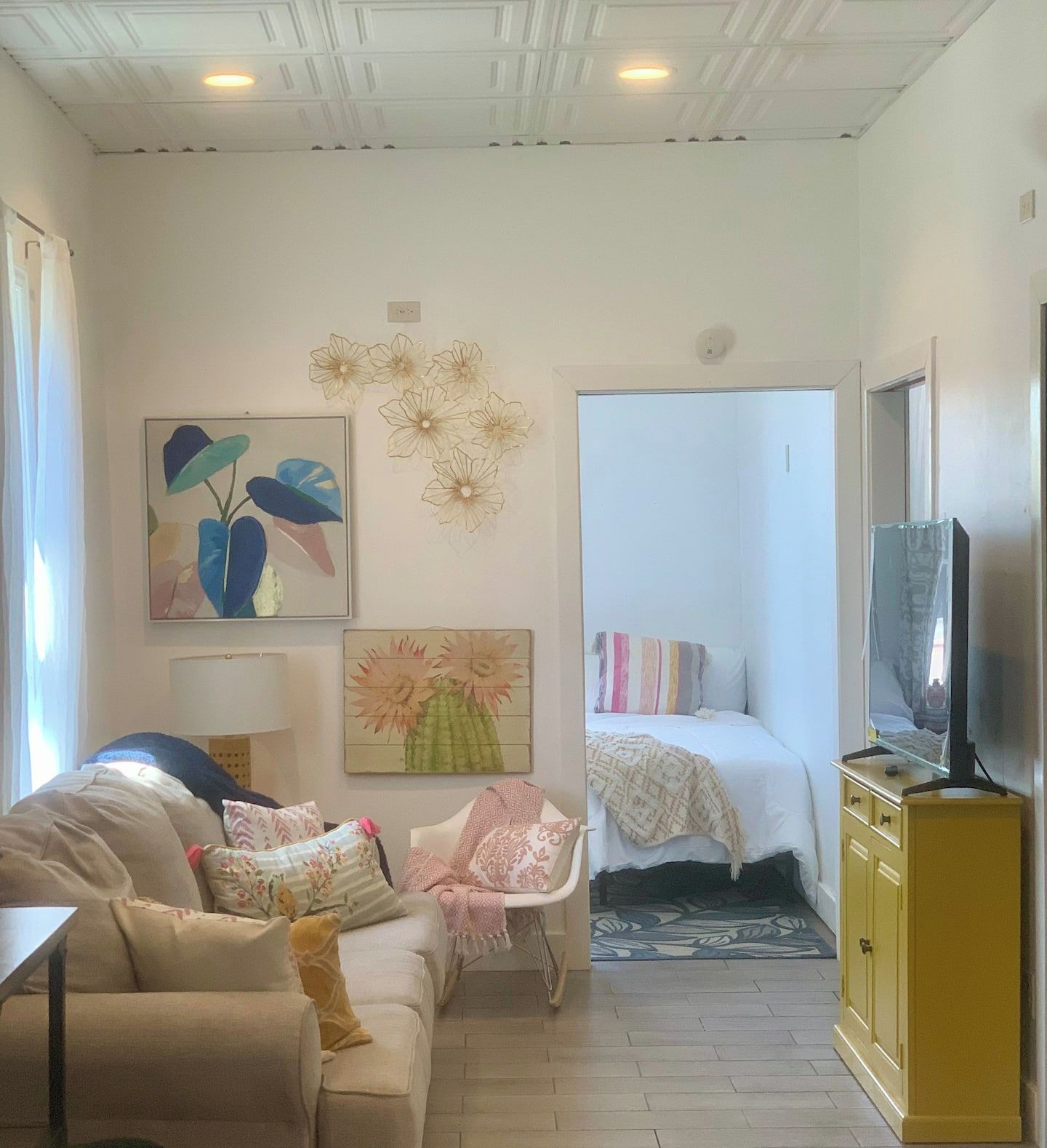 Een woonkamer met een bank, een fauteuil, een bed, een televisie en kunstwerken aan de muur.