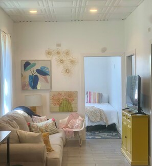 A living room with a sofa, a chair, a bed, a television, and artwork on the walls.
