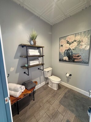 Ein Badezimmer mit einer Holzbank, einer Toilette, einem Ablagefach mit Handtüchern und einem Bild an der Wand.