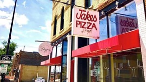 Un restaurant de pizzas avec une enseigne indiquant « Takes Pizza » et un panneau « Piste cyclable » à proximité.
