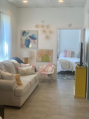 A living room with a sofa, a rocking chair, a bed with a striped pillow, and a television.