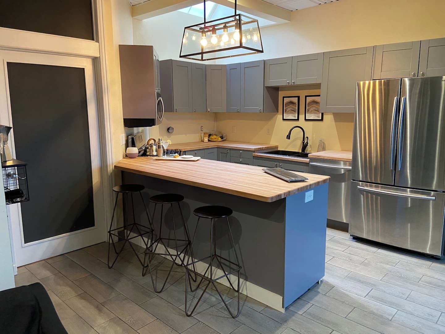 A modern kitchen with a central island, bar stools, stainless steel appliances, and a pendant light.