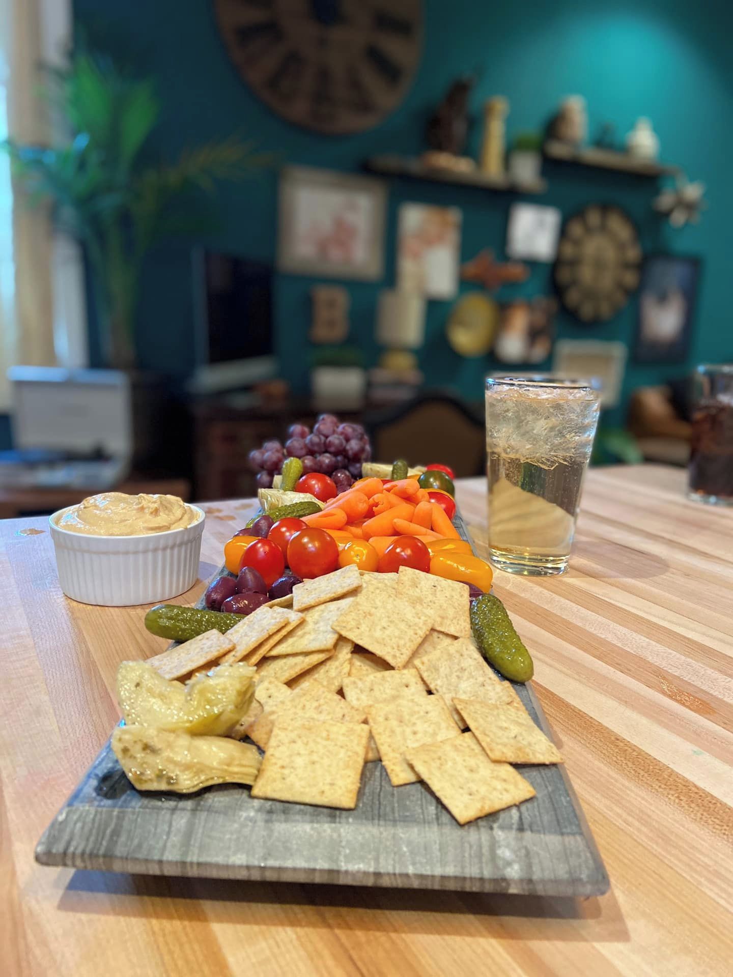 A snack platter with crackers, cheese, and vegetables on a wooden table.