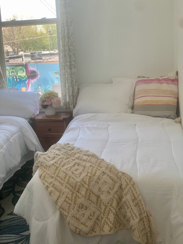 A bedroom with two beds, a nightstand with a vase of flowers, and a view of a pool through a window.