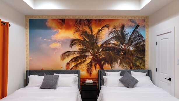 A hotel room with two beds, a nightstand, and a wall mural of palm trees and a sunset. - 10 Mins to NRG, Sleeps 12, Hot Tub, 4BR Home (Houston)
