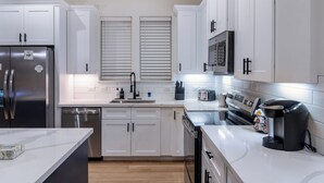 A modern kitchen with white cabinetry, stainless steel appliances, and a coffee maker. - 10 Mins to NRG, Sleeps 12, Hot Tub, 4BR Home (Houston)