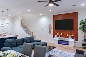 Una sala de estar moderna con un sofá seccional, un televisor de pantalla plana montado en una pared de madera, una chimenea y una escalera que conduce a un nivel superior.