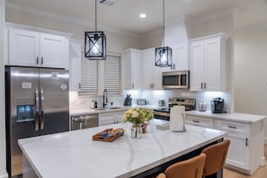 Cocina moderna con armarios blancos, electrodomésticos de acero inoxidable, una isla central e iluminación colgante.