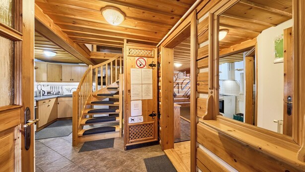 A wooden interior with a staircase leading to a second floor, a kitchen area, and a door with a no-smoking sign.