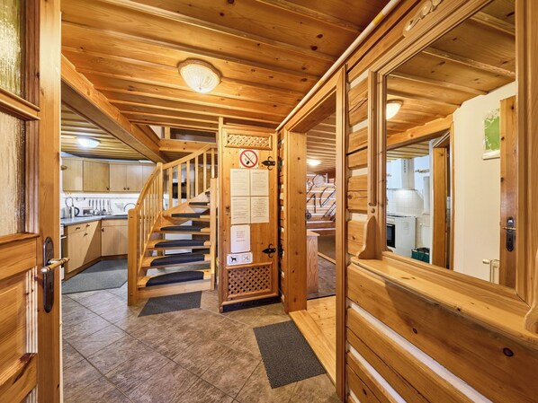 Interior de madera con una escalera que sube a un segundo piso, una zona de cocina y una puerta con un cartel de prohibido fumar.