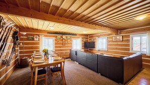 A log cabin interior with a dining area, a sofa, and a TV mounted on the wall.