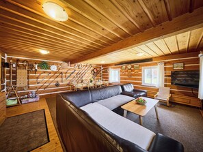 A log cabin interior with a sofa, a dining table, and a TV.