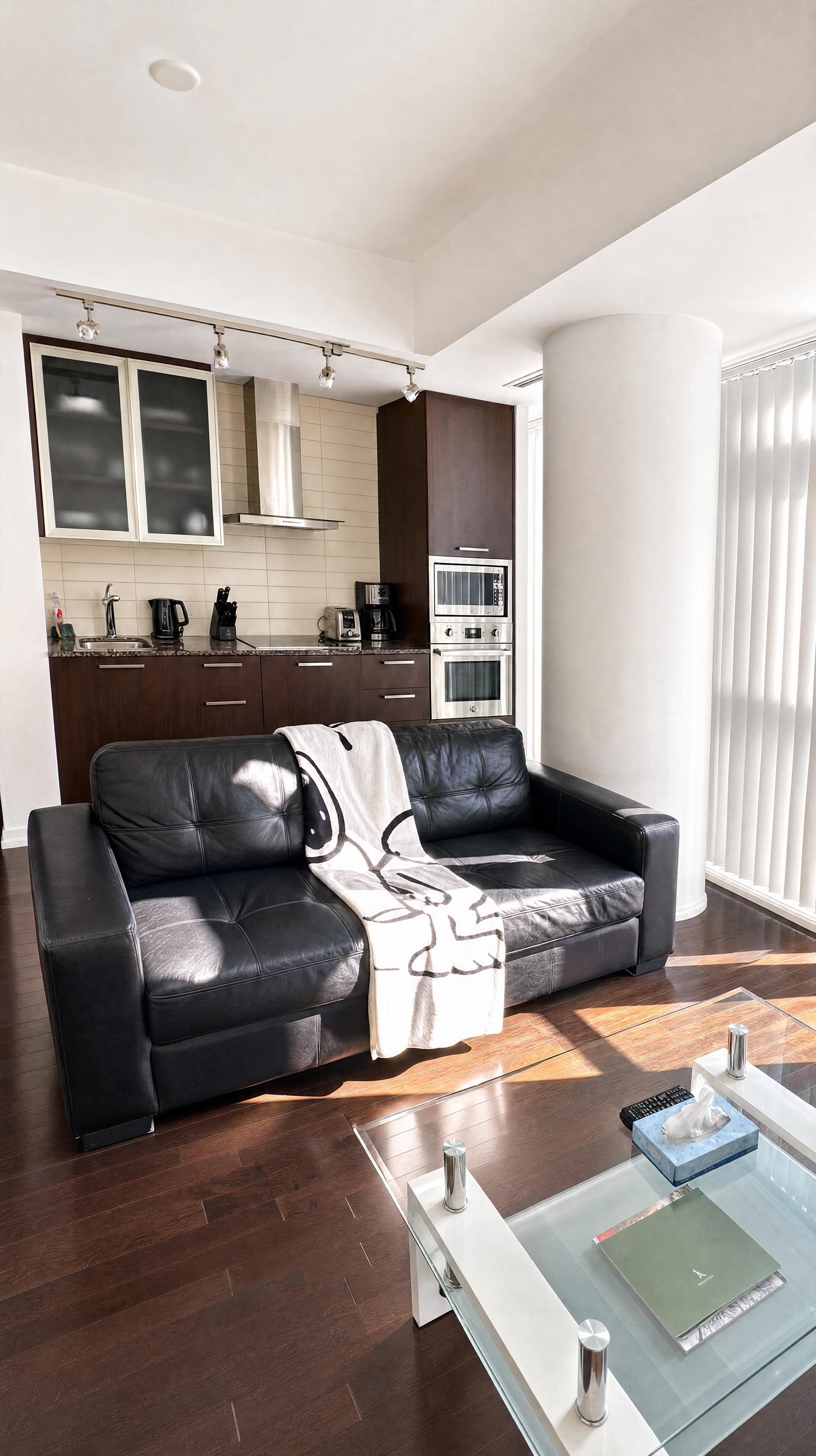 A modern living room with a leather sofa, a glass coffee table, and a kitchen in the background.