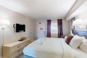 A hotel room with a bed, a television, a dresser, and a window with curtains. - Oceanfront 1BR Condo | Balcony, Pool & Views (Myrtle Beach)