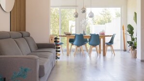 En moderne stue med sofa, spisebord med stole og et stort vindue.