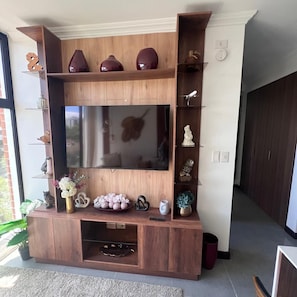 A modern living room with a large flat-screen TV, wooden entertainment unit, decorative items, and a potted plant. - Edificio Arles (Guatemala City)