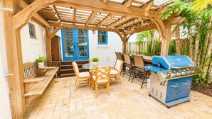 Eine überdachte Terrasse im Freien mit Grill, Sitzgelegenheiten und einer blauen Tür.