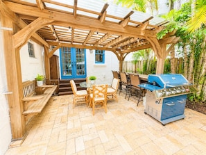 Eine überdachte Terrasse im Freien mit Grill, Sitzgelegenheiten und einer blauen Tür.