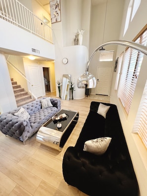 A spacious living area with a grand staircase, a black sofa, a grey sofa, and a coffee table. - Fully Furnished 3BR Home in Gated East Mesa (Mesa)