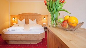 Ein Hotelzimmer mit einem hölzernen Bett, einem Nachttisch mit Lampe, einer Vase mit Blumen und einer Obstschale.