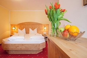 A hotel room with a wooden bed, a nightstand with a lamp, a vase with flowers, and a fruit bowl. - New four star apartment no. 7 with 52 square meters, Die Bequeme (Gstadt am Chiemsee)