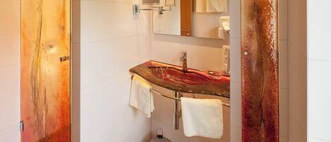 A modern bathroom with a glass shower enclosure, a stainless steel sink, and a trash bin.