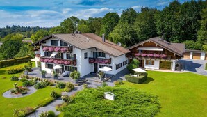 A two-story chalet with a balcony, surrounded by a well-maintained garden and a forested backdrop. - New four-star vacation apartment with 42 sqm No. 3, The Sunny One (Gstadt am Chiemsee)