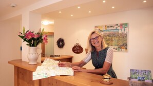 A reception desk with a vase of flowers, a bulletin board with various notices, and a wooden counter. - New four-star vacation apartment with 42 sqm No. 3, The Sunny One (Gstadt am Chiemsee)