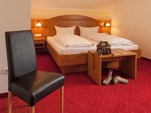 Ein Hotelzimmer mit Bett, Stuhl, Nachttisch mit Lampe und einem Paar Schuhen auf dem Boden.