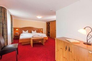 Ein Hotelzimmer mit Bett, Holz-Kopfteil, Schreibtisch mit Lampe, Kleiderschrank und rotem Teppich.