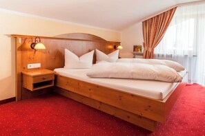 Ein Hotelzimmer mit einem hölzernen Bett, zwei Nachttischen, einem roten Teppich und einem Fenster mit Vorhängen.