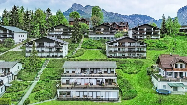 Eine Wohngegend an einem Hang mit mehreren zweistöckigen Häusern, die alle Balkone und einen Blick auf die umliegende Natur und Berge bieten.