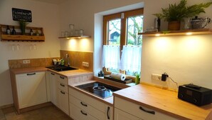 A kitchen with a sink, stove, wooden cabinets, and a window with curtains. - Vacation apartment "Wendelsteinblick" (Heufeld)
