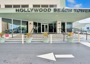 Der Eingang zum Hollywood Beach Tower mit freiem Blick auf den Schriftzug des Gebäudes, einer Treppe, die zum Eingang führt, und Richtungspfeilen auf dem Boden.