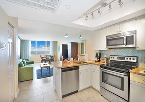 Eine moderne Küche mit Edelstahlgeräten, ein Essbereich mit einem grünen Sofa und ein Blick auf den Himmel durch große Fenster.