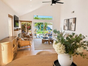 A spacious living area with a wooden coffee table, leather sofa, and a large window offering a view of a garden. - San Clemente Beach Retreat / Fire Pit  Patio  Indoor-Outdoor Living (San Clemente)