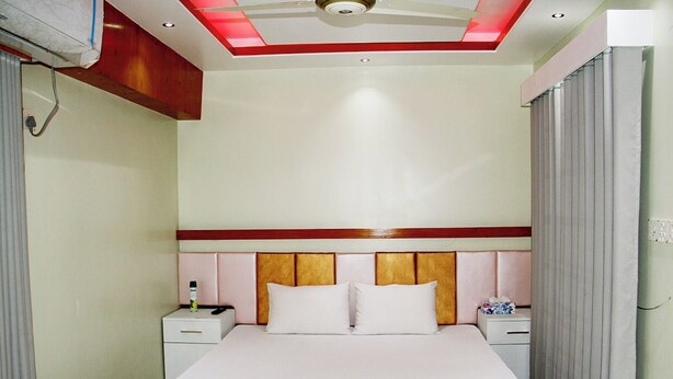 Een hotelkamer met een bed, twee nachtkastjes, een ventilator aan het plafond en een raam met gordijnen.