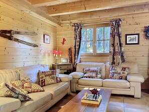 A cozy cabin interior with a wooden ceiling, two leather sofas with patterned cushions, a chessboard on a wooden coffee table, and a window with curtains. - La Suisse Normande by Interhome (Les Diablerets)