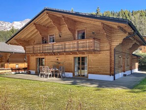 Eine Holzhütte mit Balkon, einem Essbereich mit Stühlen und Tisch sowie einem Blick auf die Berge.