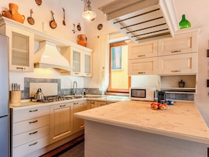 A kitchen with a central island, wooden cabinets, a stove, and a microwave. - La Terrazza sul Lago by Interhome (Dervio)