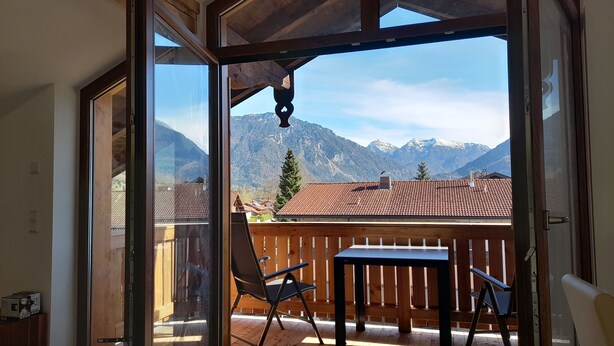 Quarto com teto de madeira, porta de vidro deslizante que dá para uma varanda externa com mesa e cadeiras, e vista para as montanhas.